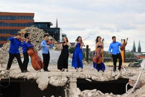 Sieben Musikerinnen und Musiker vom Kammerensemble Konsonanz stehen mit ihren Streichinstrumenten auf einer Baustelle.