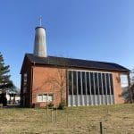 Kleine Backsteinkirche mit schwarzem Dach und rundem Turm.