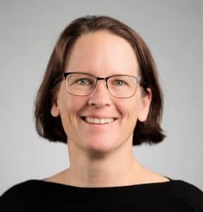 Katrin Anders, kinnlange braune Haare und Brille, schaut freundlich lächelnd in die Kamera.